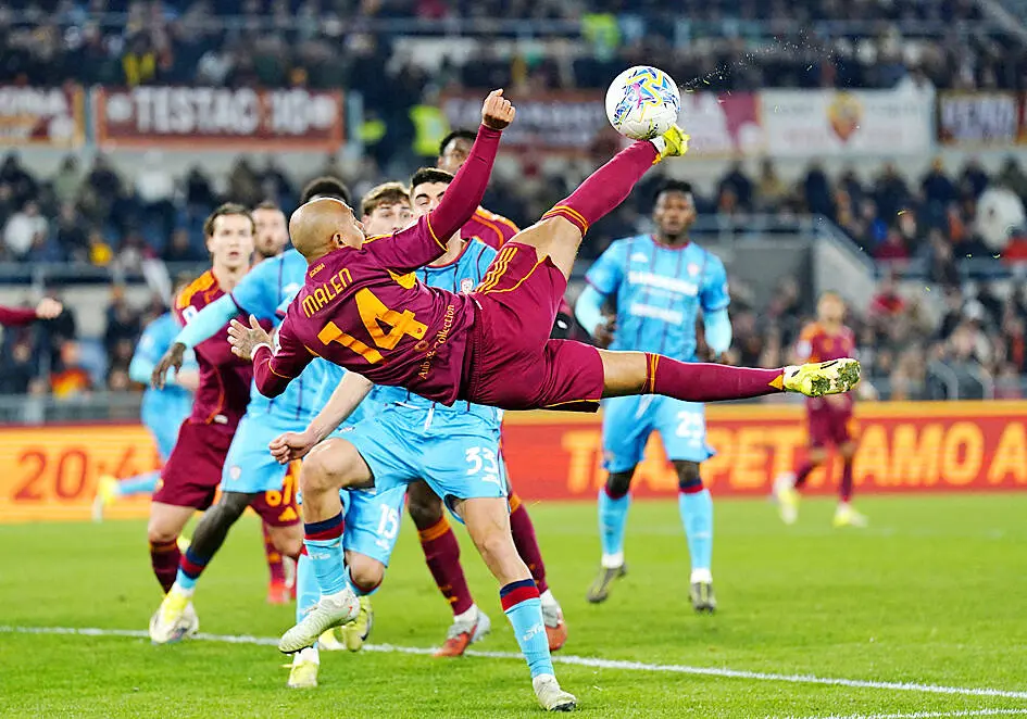 Donyell Malen in a maroon AS Roma kit performing a bicycle kick during a football match