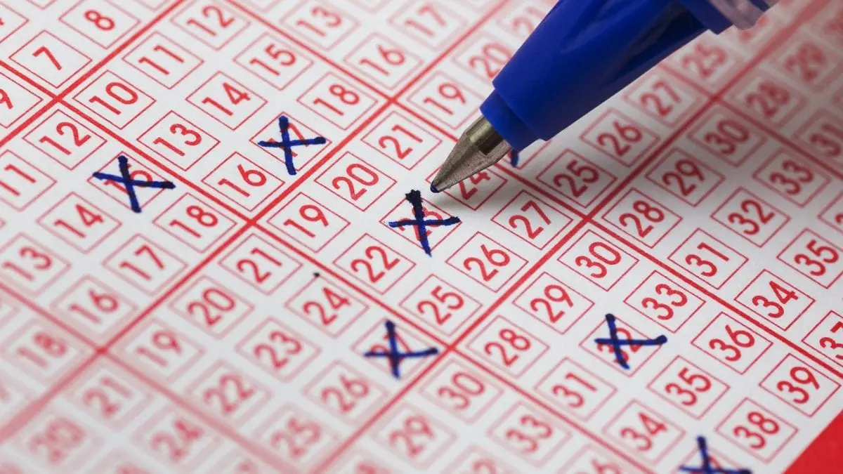 Close-up of a blue pen marking numbers with crosses on a red and white lottery betting slip
